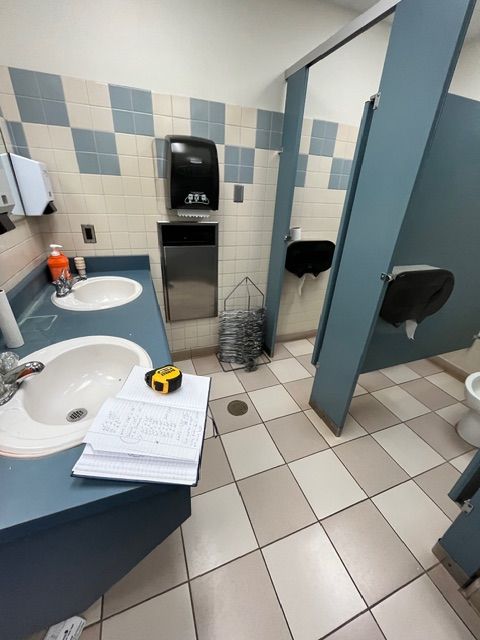 Public restroom with sinks, stalls, and tiled floor; blue and white color scheme.