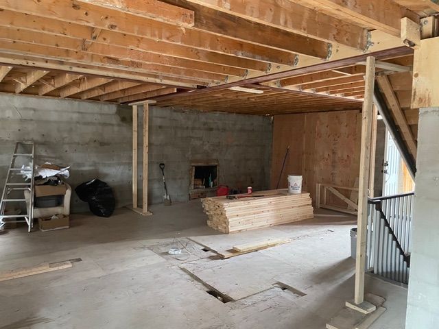 Basement under construction: wood framing, concrete walls, ladder, lumber, unfinished ceiling.