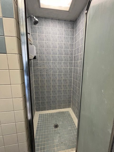 A tiled shower stall with a glass door and overhead showerhead.
