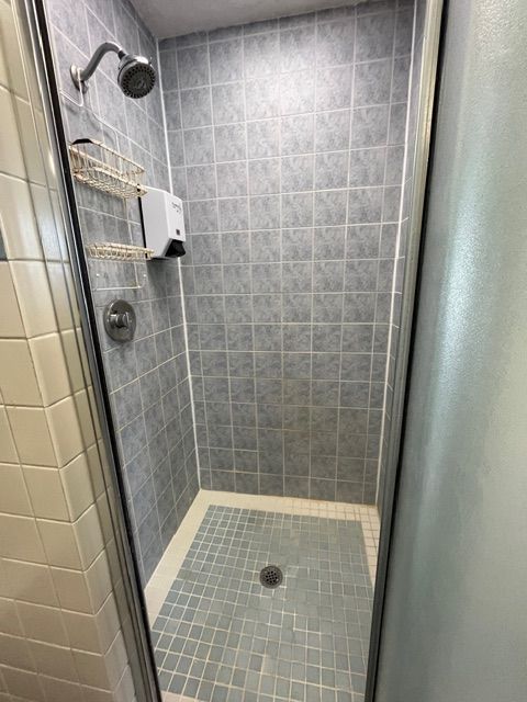 Small shower with gray tiled walls and floor, silver shower head, and glass door.
