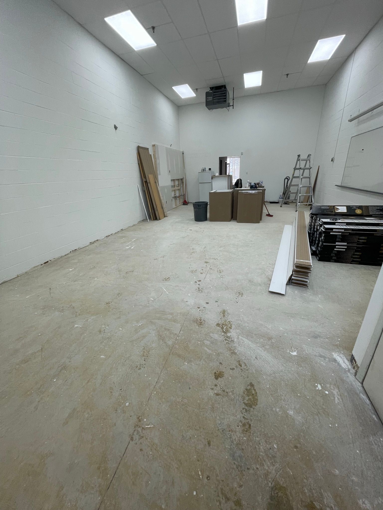 Empty room with white walls, fluorescent lights, and construction materials scattered on the floor.