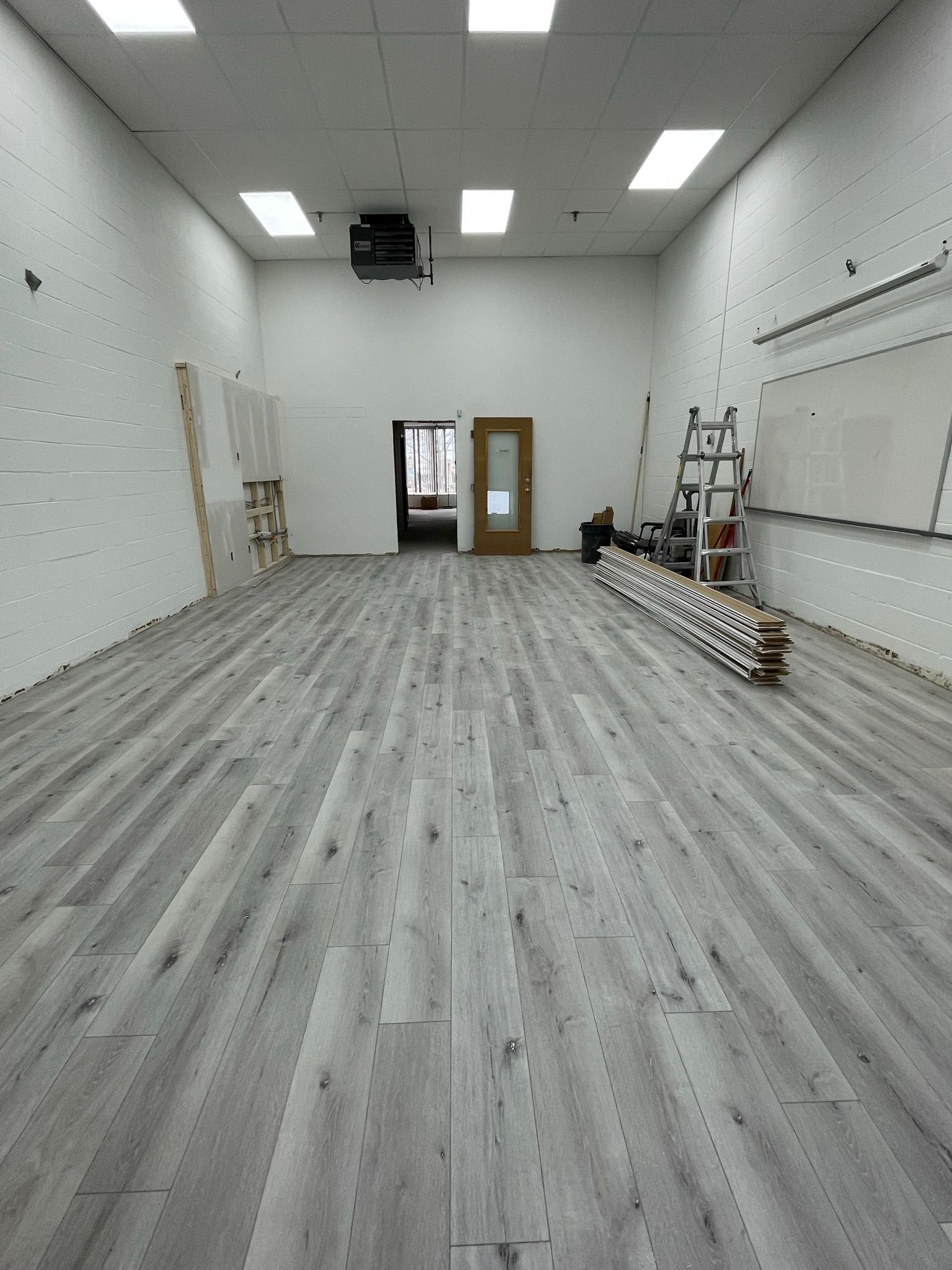 Empty room with light gray wood-look flooring, white walls, and a door at the far end.