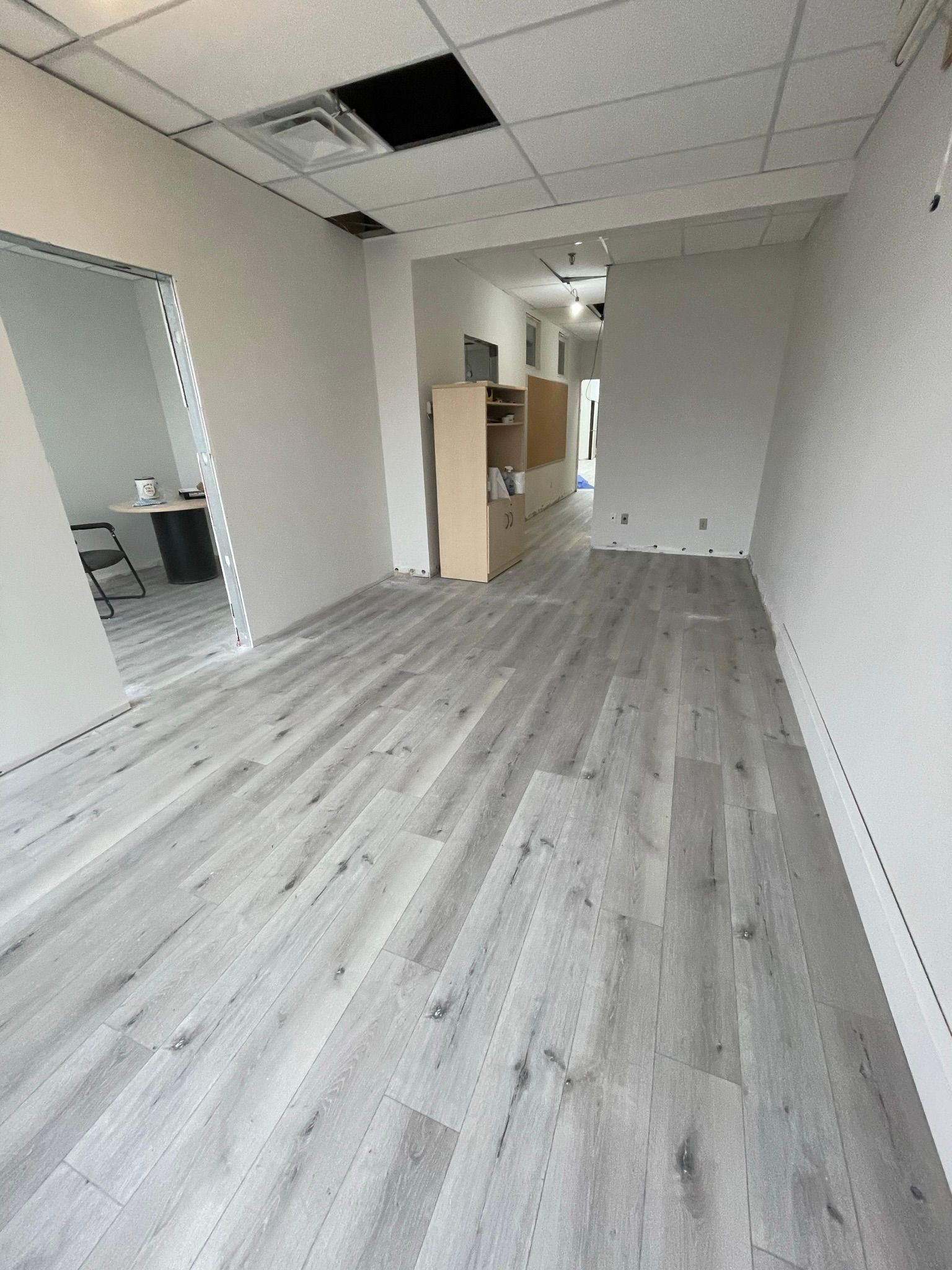 Empty, renovated interior space with gray wood-look flooring and white walls.