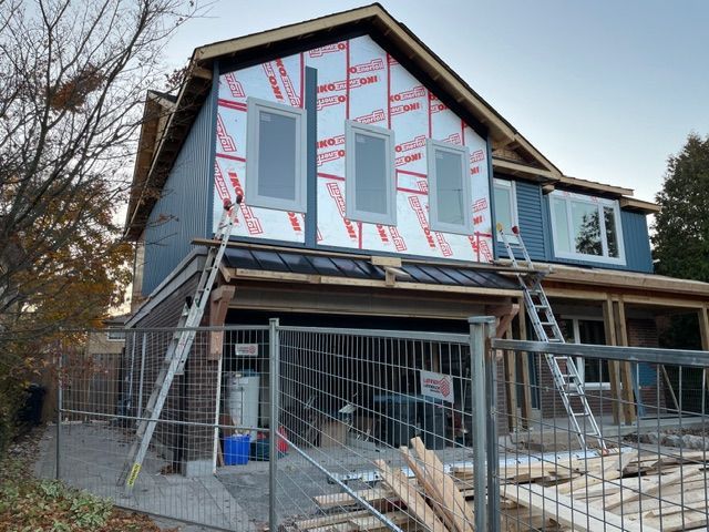 House under construction with blue siding, exposed insulation, windows, and ladders.