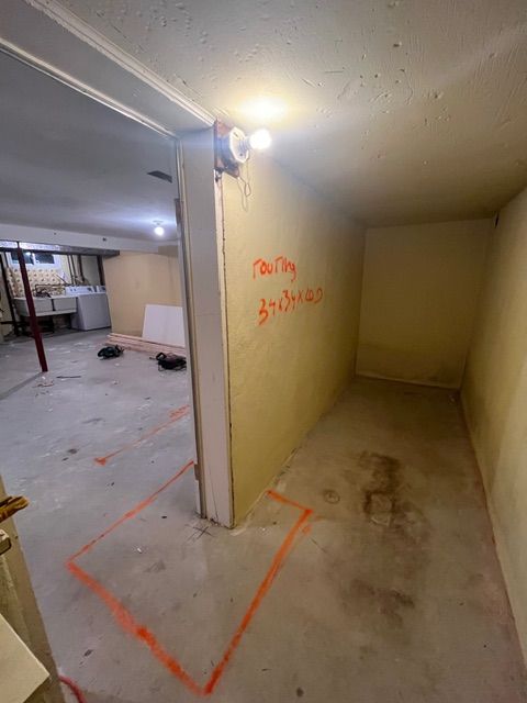 Basement with a small room. Orange spray paint outlines, writing on the wall, overhead lights.