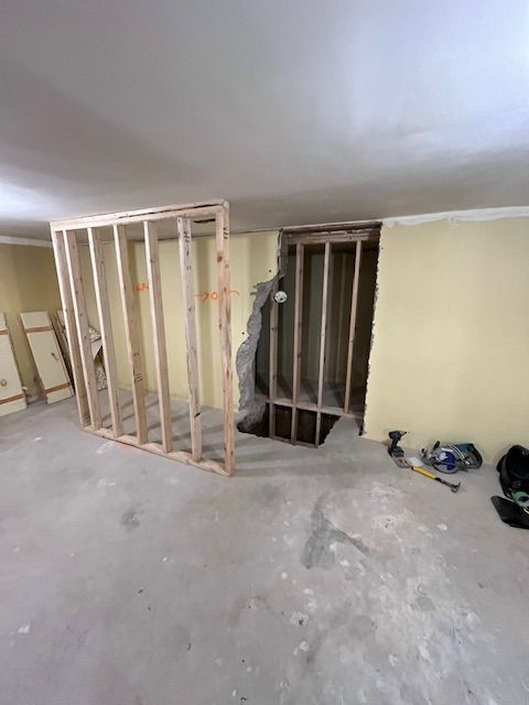 Interior construction scene: wooden wall framing in front of an unfinished opening; yellow walls, concrete floor.
