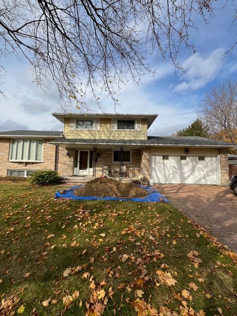 House exterior with a two-story section, brick and siding. Lawn with fallen leaves, driveway, blue tarp covering dirt.