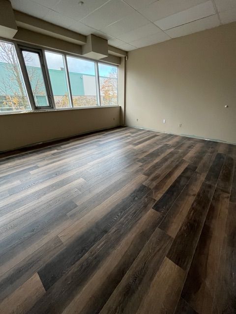 Empty room with dark wood-look flooring, large windows, and beige walls.