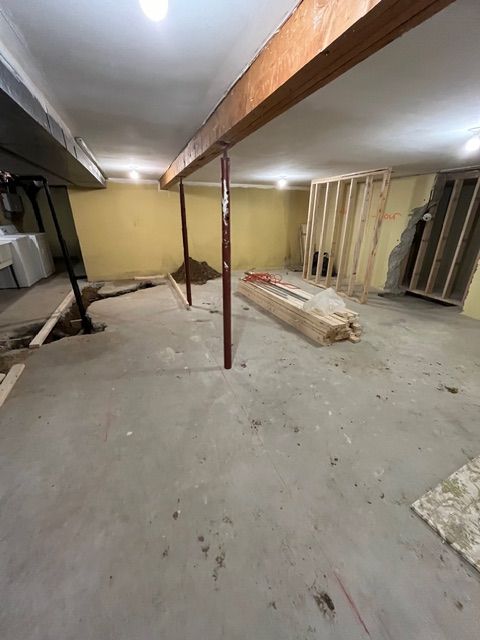 Basement under construction with exposed beams, support posts, and framed walls; dirt and concrete flooring.