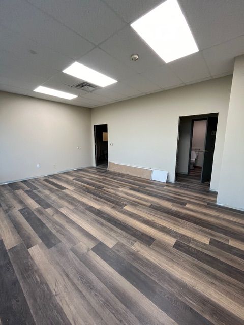 Empty office room with wood-look flooring, two doorways, and recessed lighting.