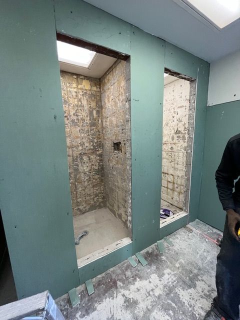 Bathroom remodel in progress with two shower stalls framed, walls covered in green drywall.