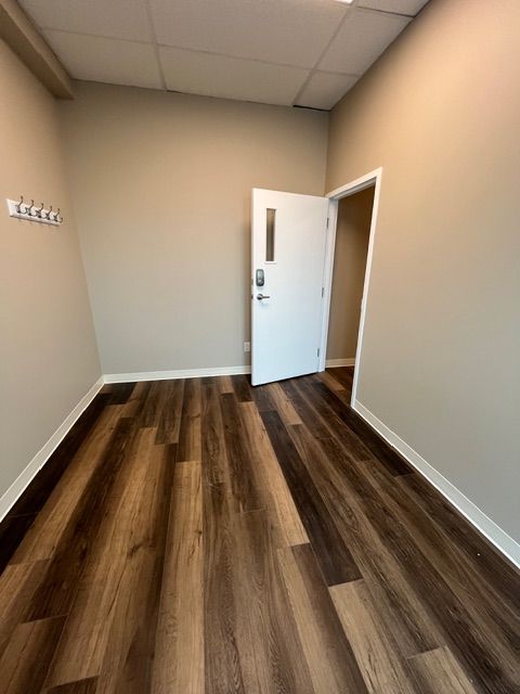Empty room with wood-look flooring, tan walls, and a white door slightly ajar. A row of hooks is on the left wall.