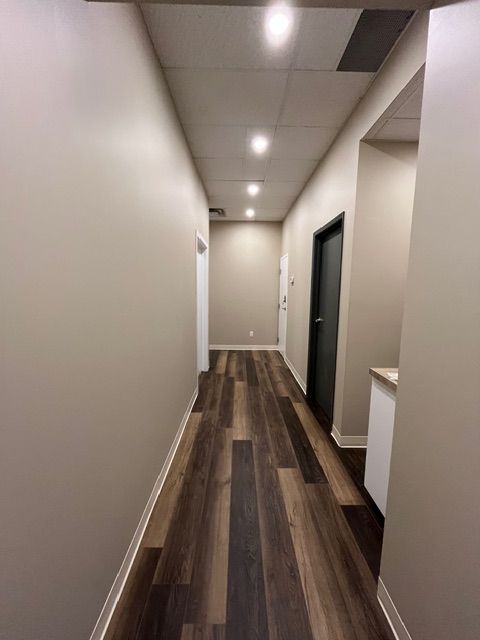 Narrow hallway with brown and gray wood-look floor, beige walls, and recessed ceiling lights. Two doors visible.