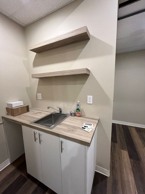 Small kitchenette with a sink, white cabinets, wooden countertops, and floating shelves. Dark wood-look flooring.