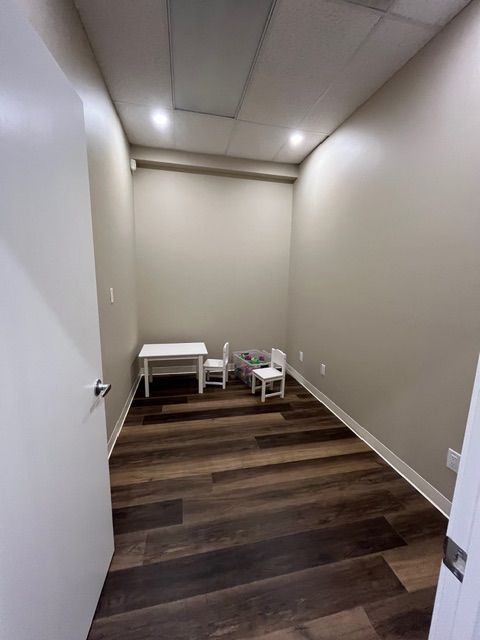 Empty playroom with wood floors, white table, and two small chairs. Neutral walls, recessed lighting.