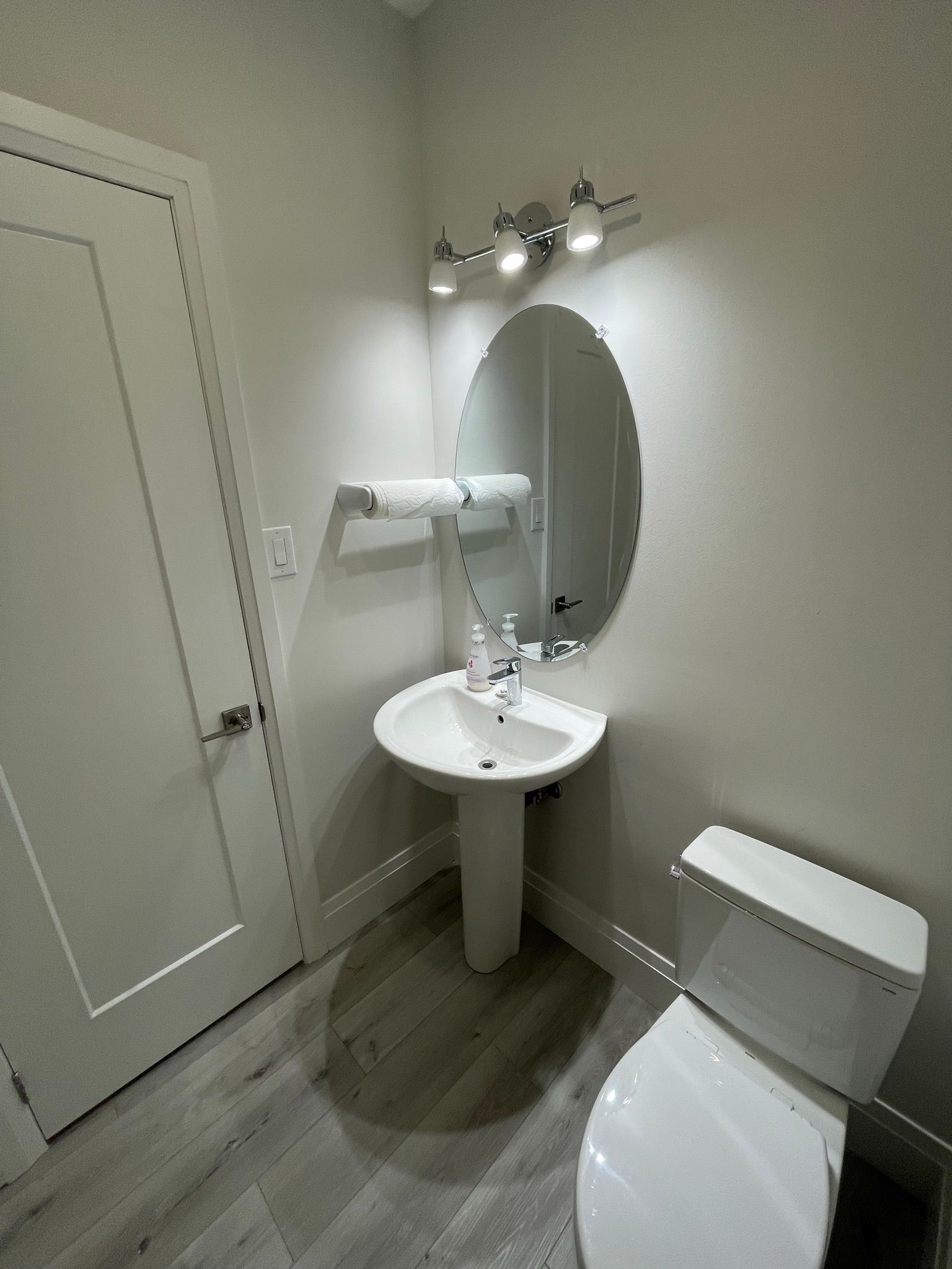 Small bathroom with white pedestal sink, oval mirror, and toilet.