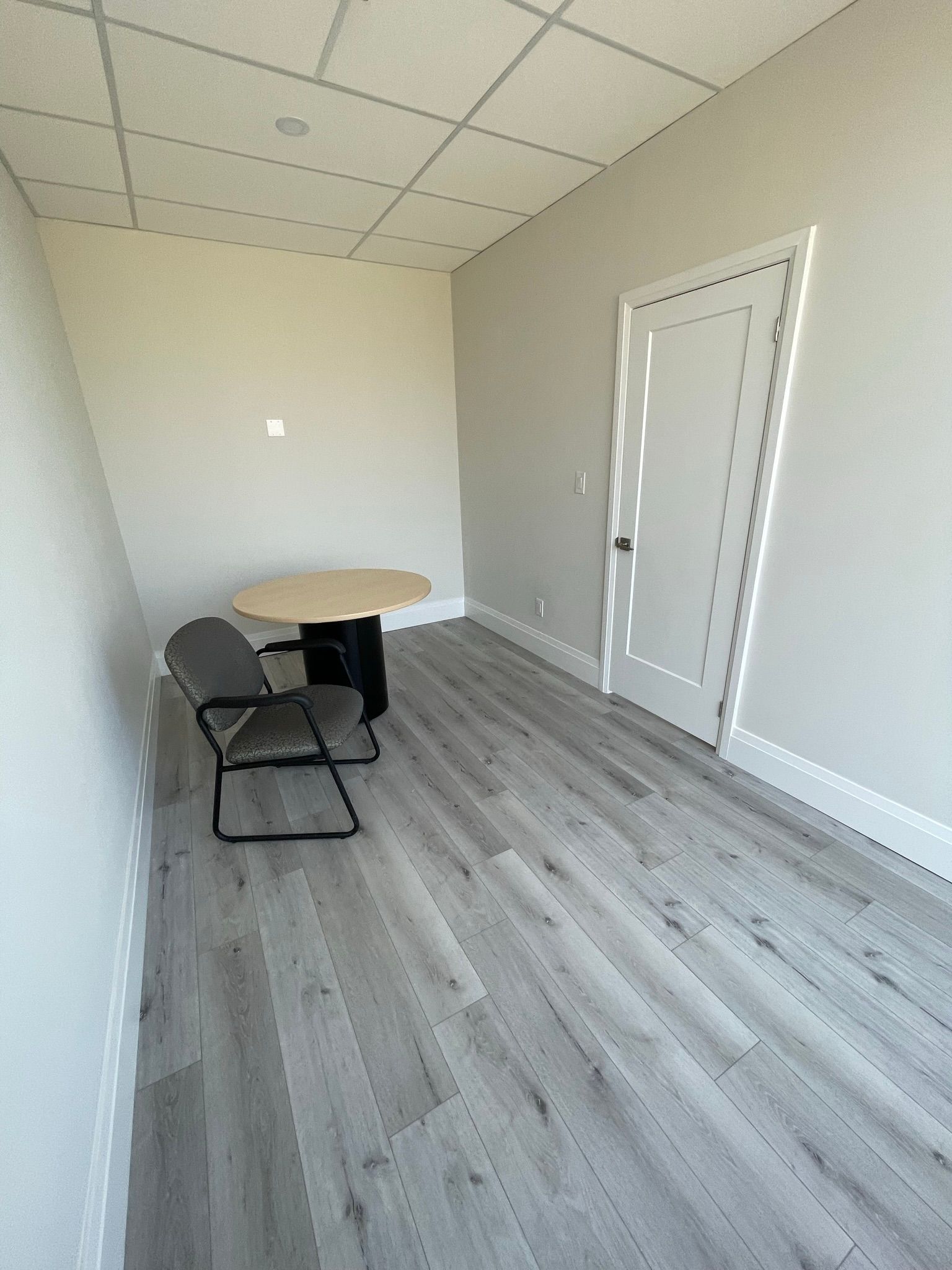 Empty office with a table, chairs, door, and gray wood-look flooring.