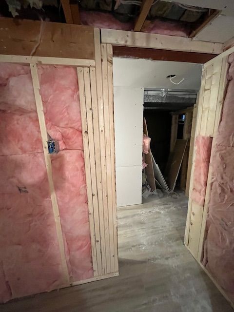 Interior view of a room under construction with exposed pink insulation and a doorway.