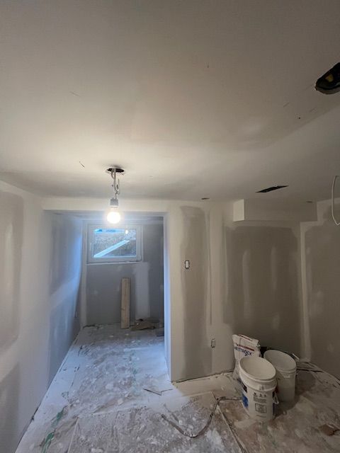 Room under construction, drywall installed on walls and ceiling. Buckets, debris, and a window are visible.