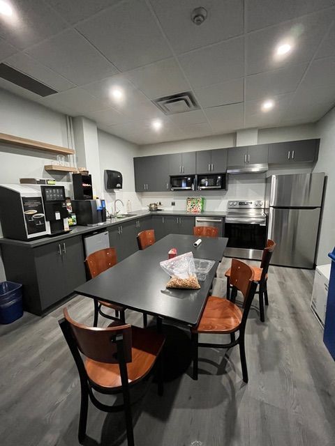 Kitchen with grey cabinets, appliances, a long black table, and brown chairs.