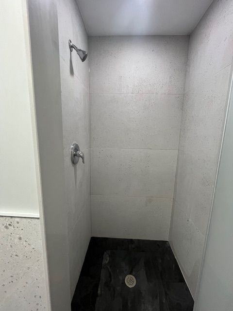A small, tiled shower with a dark floor, silver fixtures, and light-colored walls.