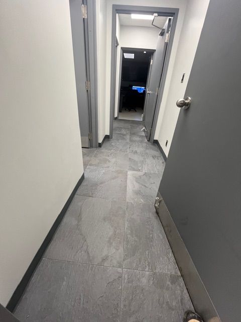 Narrow hallway with gray tile floor, white walls, and gray doors.