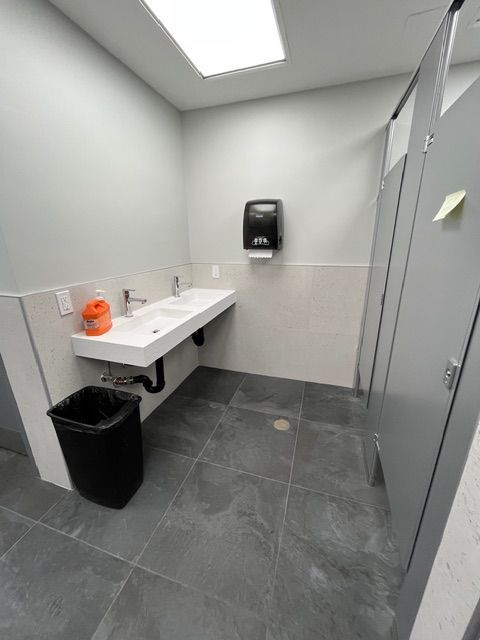 Public restroom with white sink, black trash can, and gray stalls.