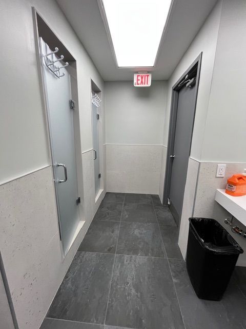 Narrow restroom hallway with two shower stalls, a closed door, and an exit sign.
