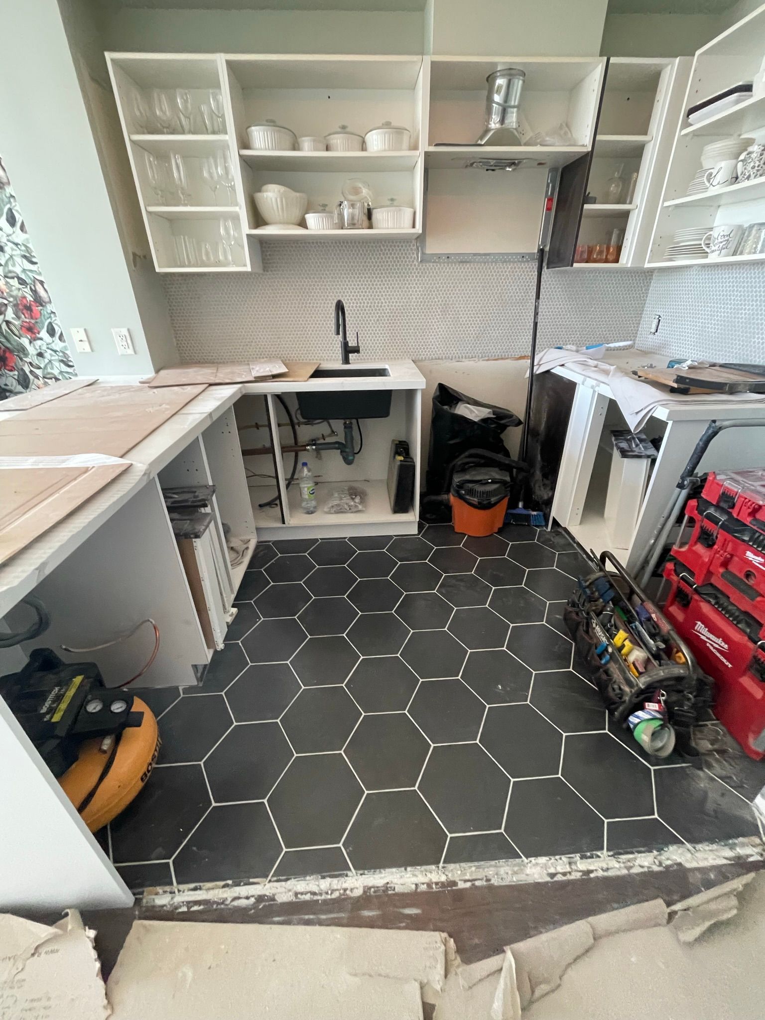 A kitchen under construction with a black tile floor and white cabinets.