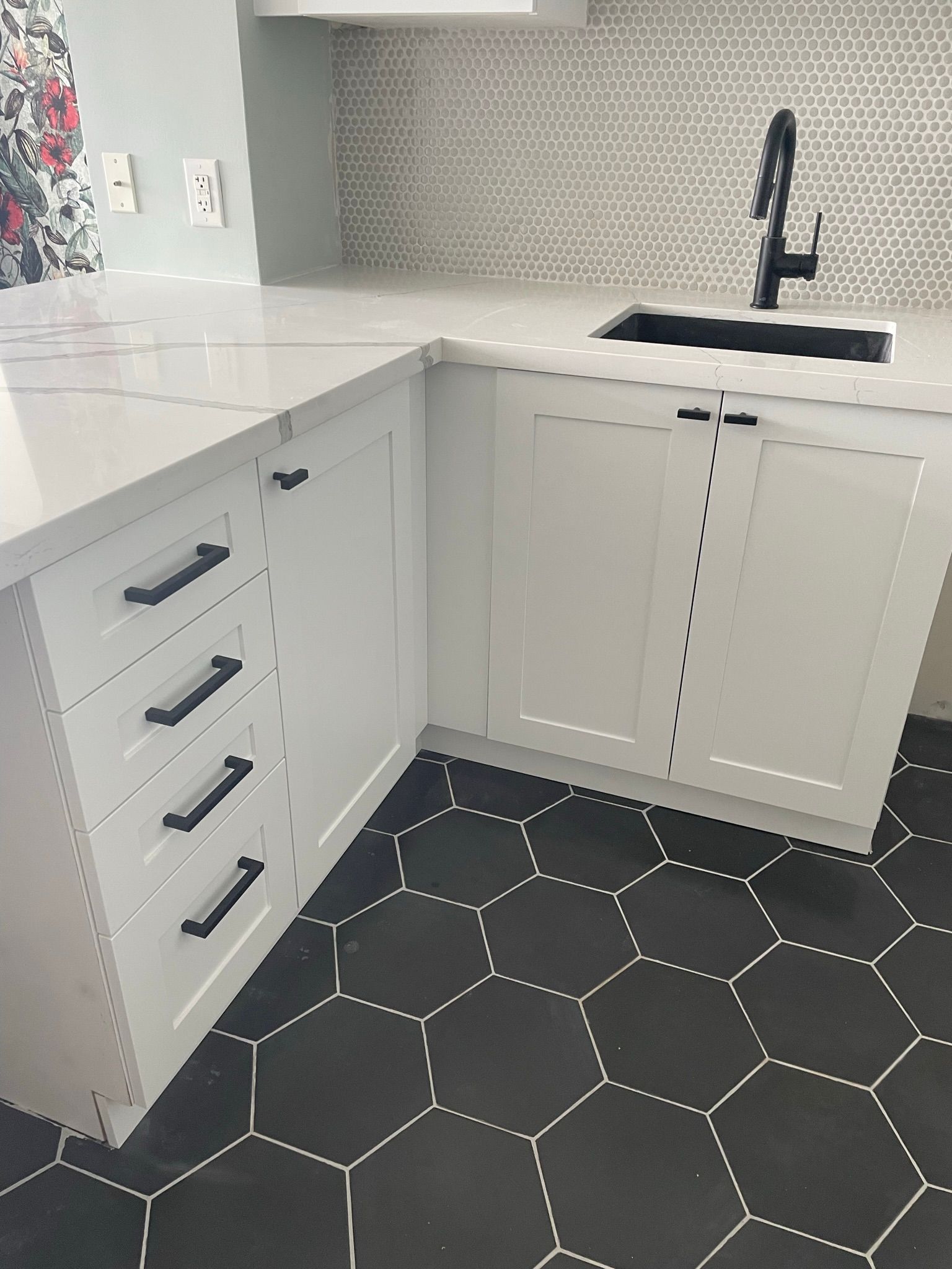 A kitchen with white cabinets and black tiles and a sink.