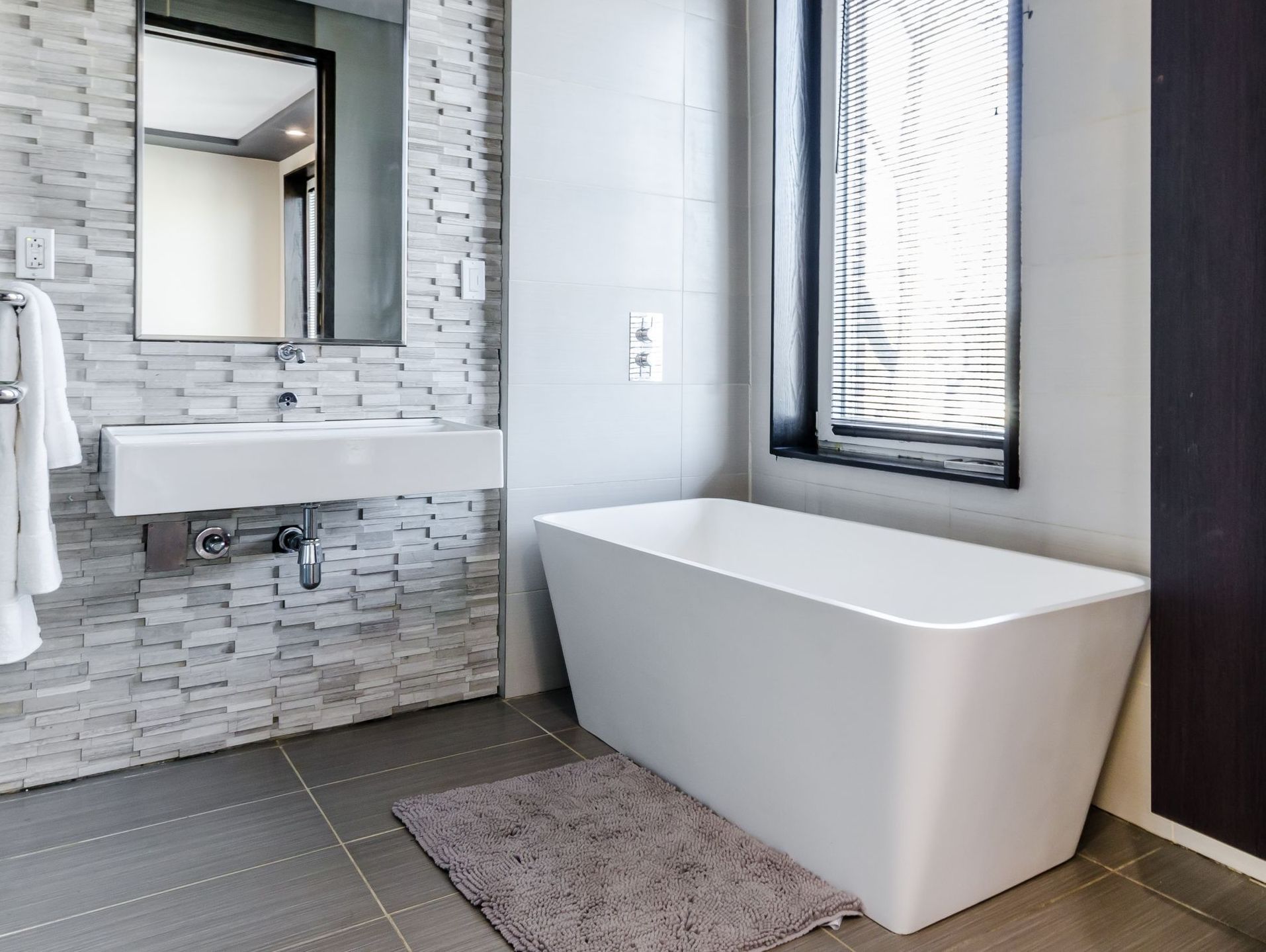 A bathroom with a bathtub , sink , mirror and window.