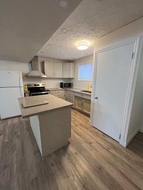 A kitchen with light gray cabinets, stainless steel appliances, and a central island with a light-colored countertop.
