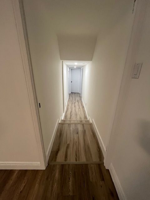Narrow hallway with wooden floor. White walls and door at end.