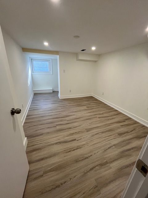 Empty room with wood-look flooring, white walls, and a small window.