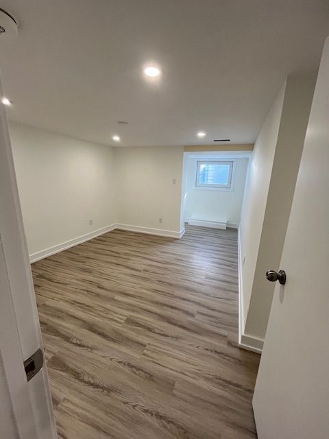 Empty, bright room with wood-look flooring and white walls. Light enters from a window.