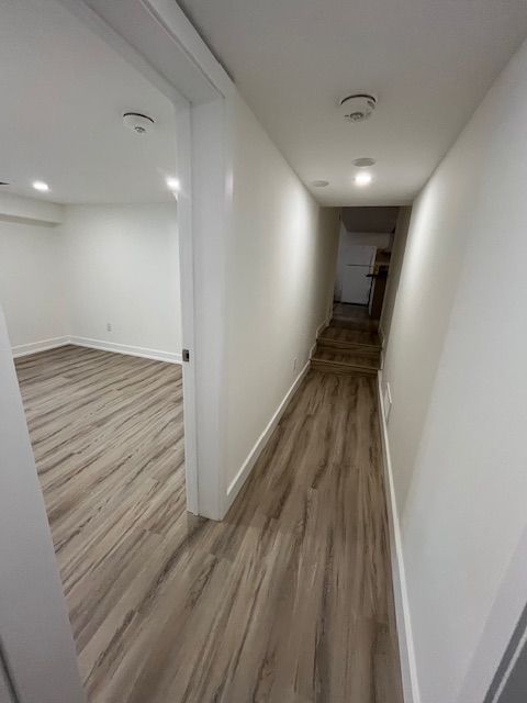 Hallway with wood-look flooring and white walls, leading to a staircase and room.