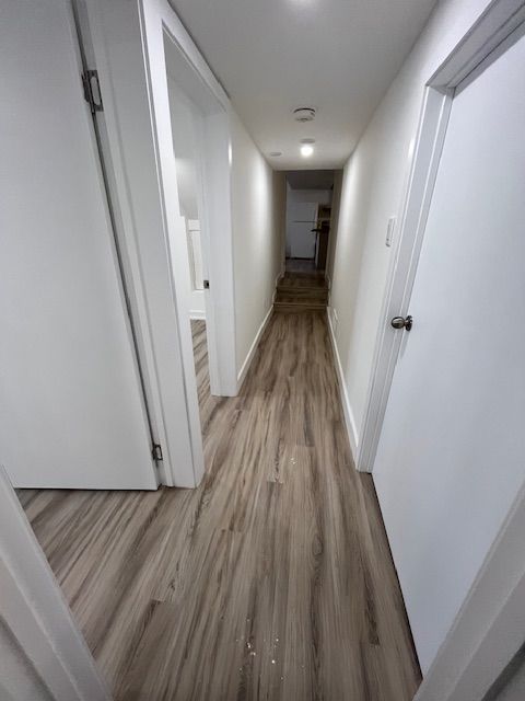 Narrow hallway with light wood-look flooring, white walls, and white doors leading to rooms.
