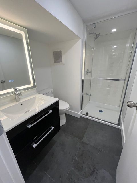 Modern white bathroom with black vanity, toilet, and glass shower. Slate gray floor.