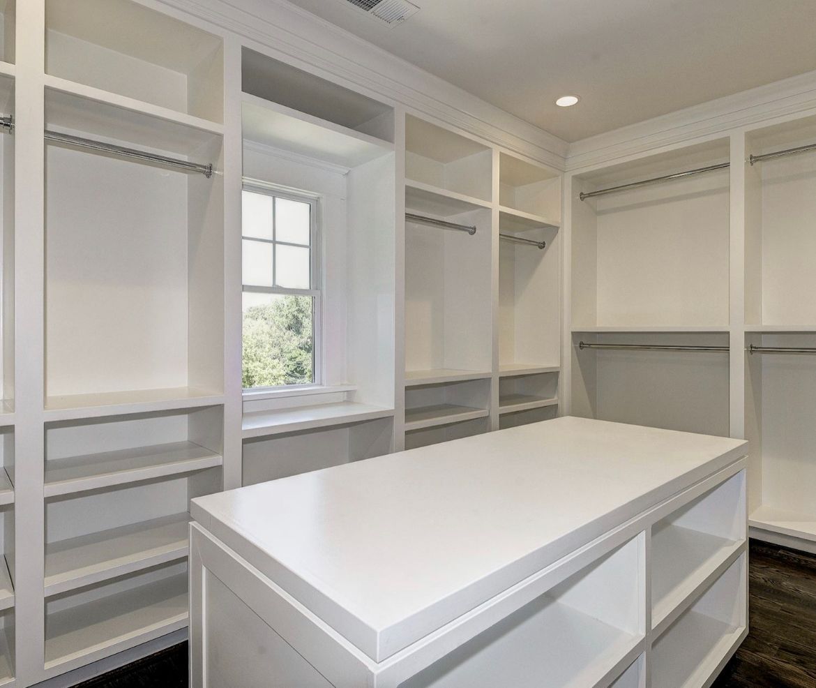 A walk in closet with lots of shelves and a large white table.