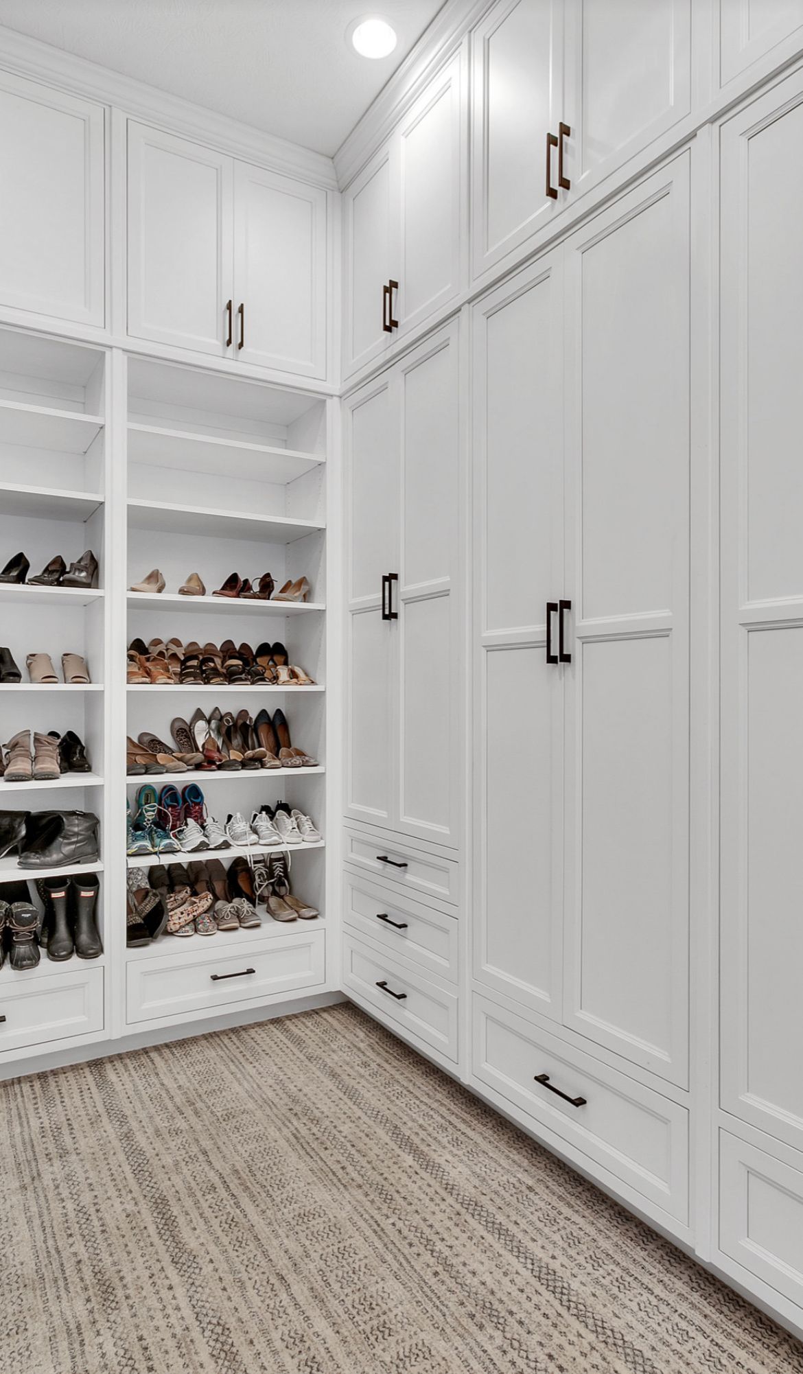 A walk in closet with white cabinets and shelves filled with shoes.