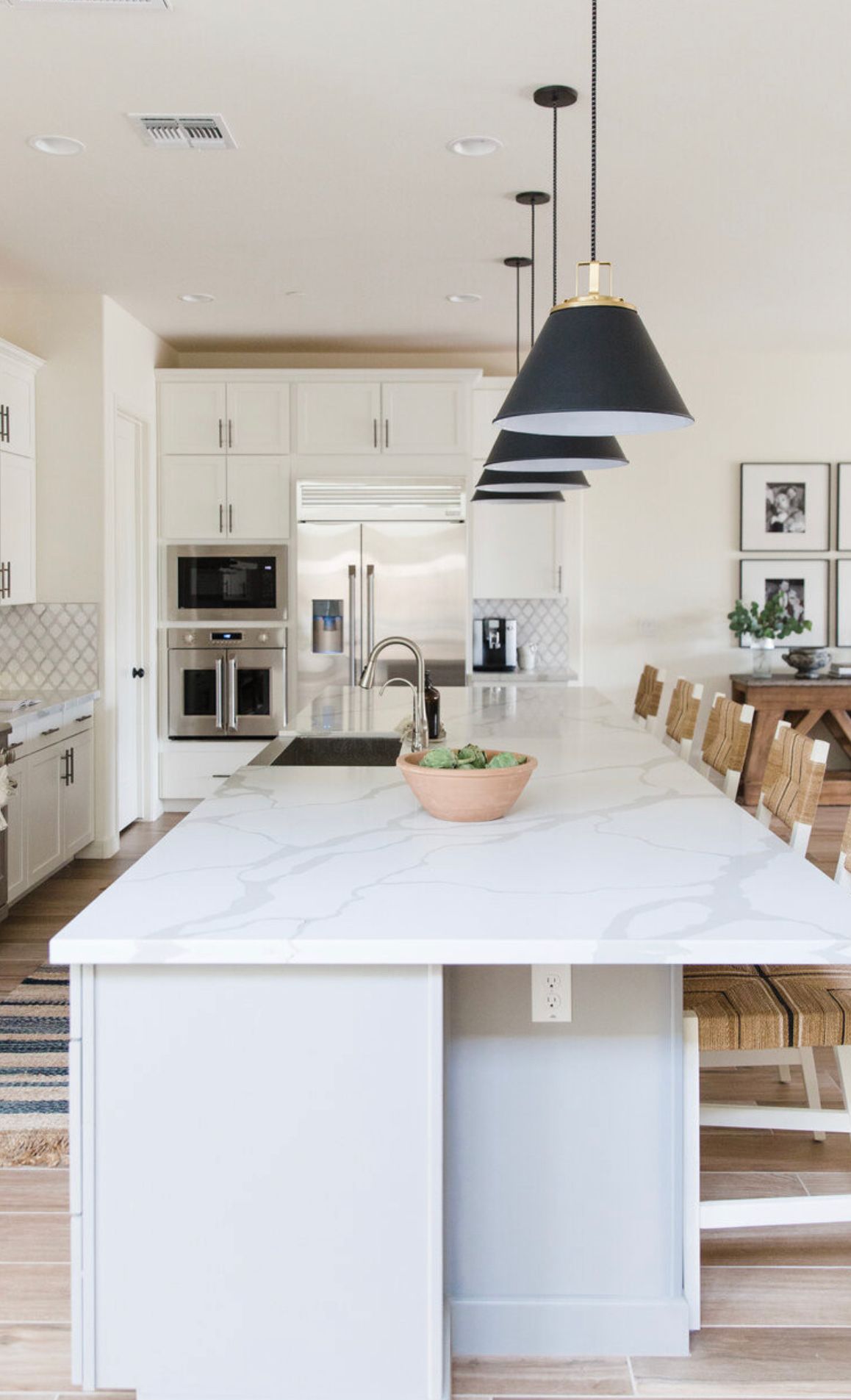 A kitchen with white cabinets , a large island , a sink , and a microwave.