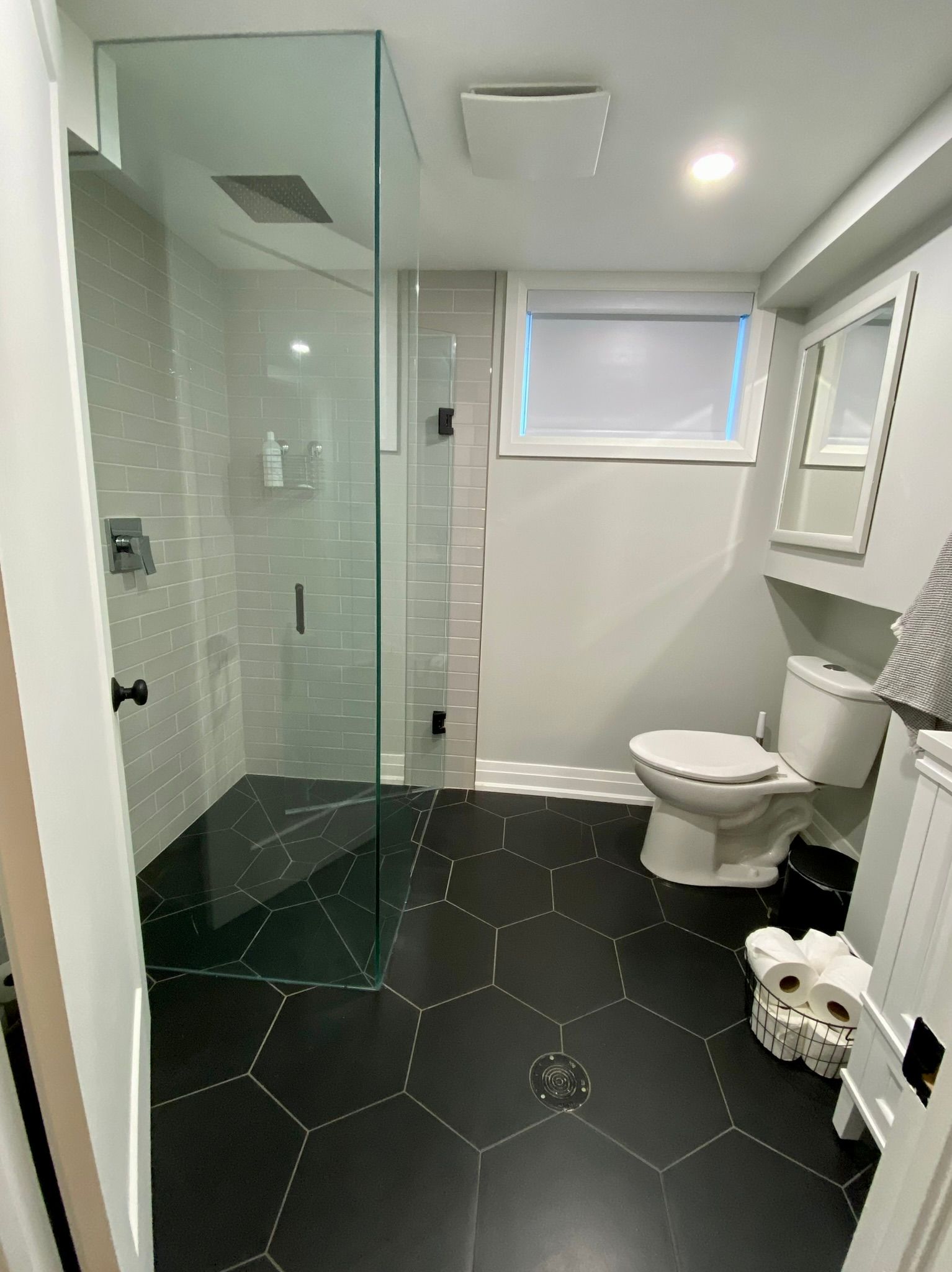 Modern bathroom with black hexagon tile floor, glass shower, and white toilet.