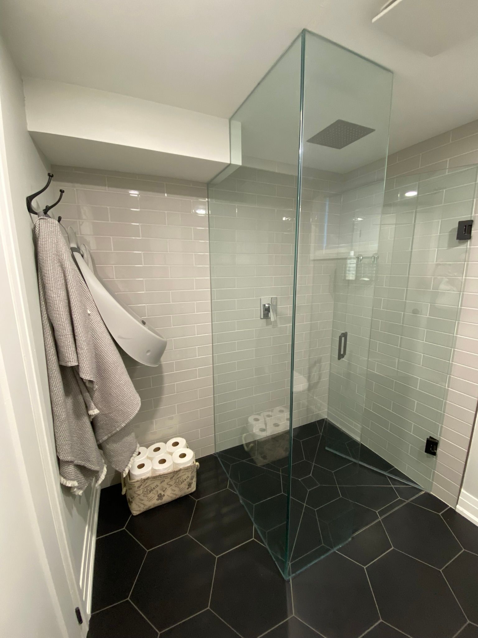 Modern bathroom with glass shower, grey tiles, black hexagonal floor, and towels on a hook.