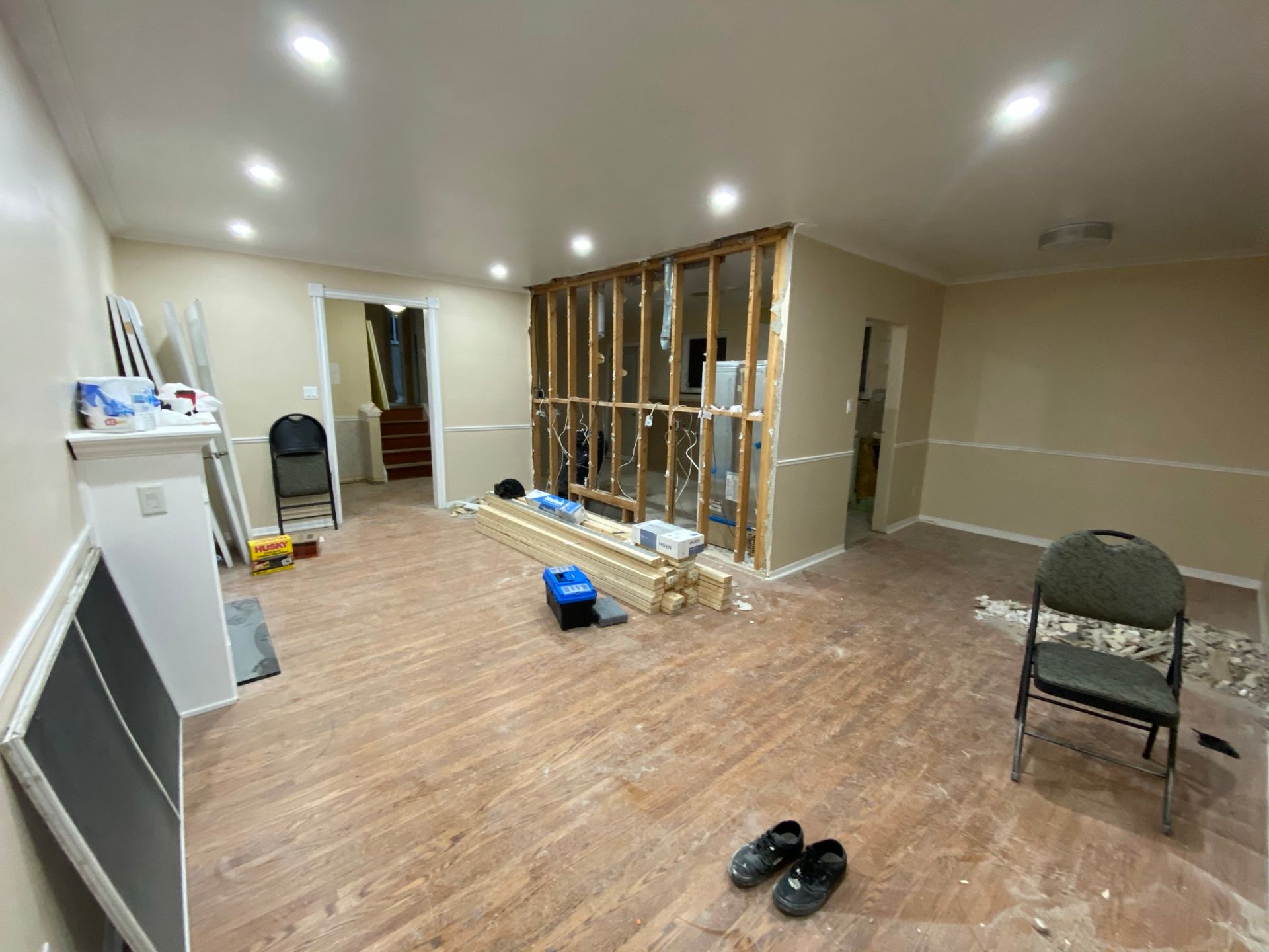 Interior room undergoing renovation, with exposed wall studs and debris. Beige walls, wood-look flooring.