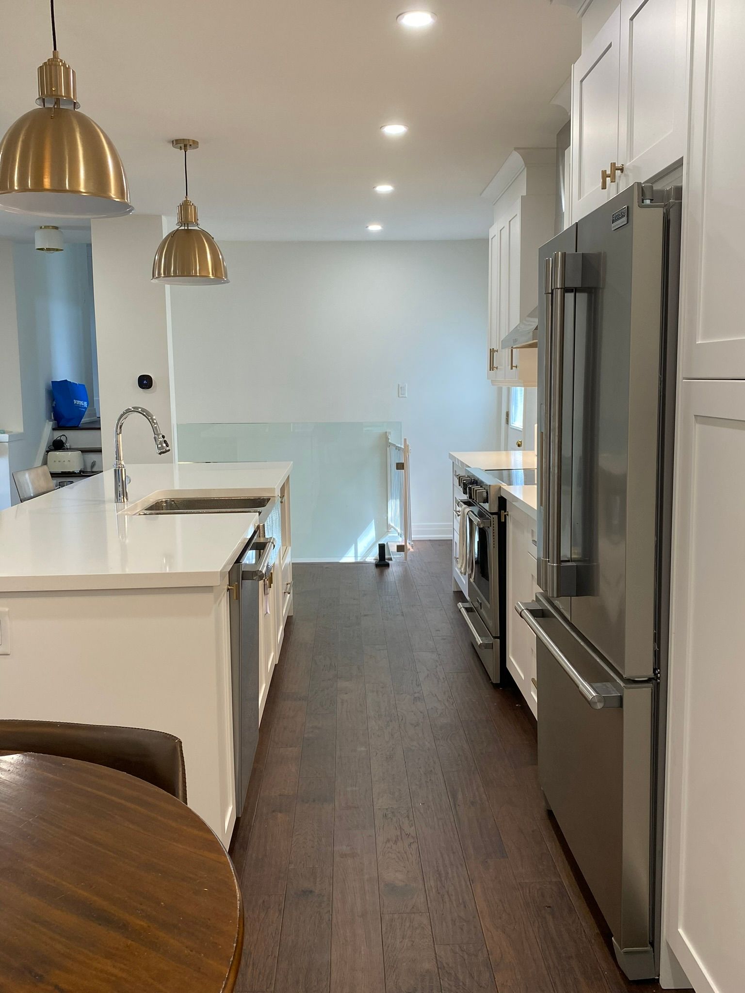 Modern white kitchen with a stainless steel refrigerator, dark wood floors, and gold pendant lights.