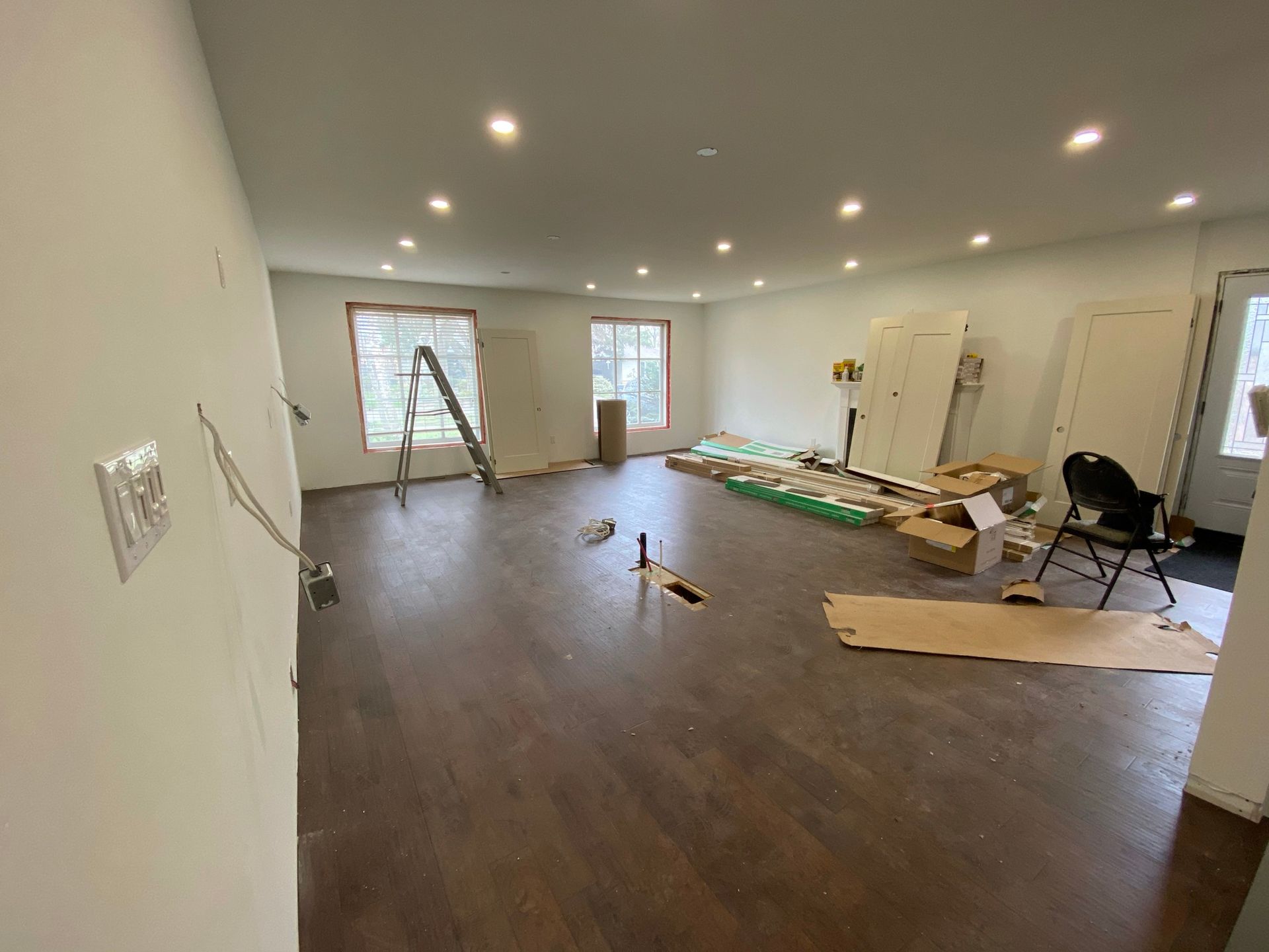 Room with wooden floor, white walls, and scattered construction materials.