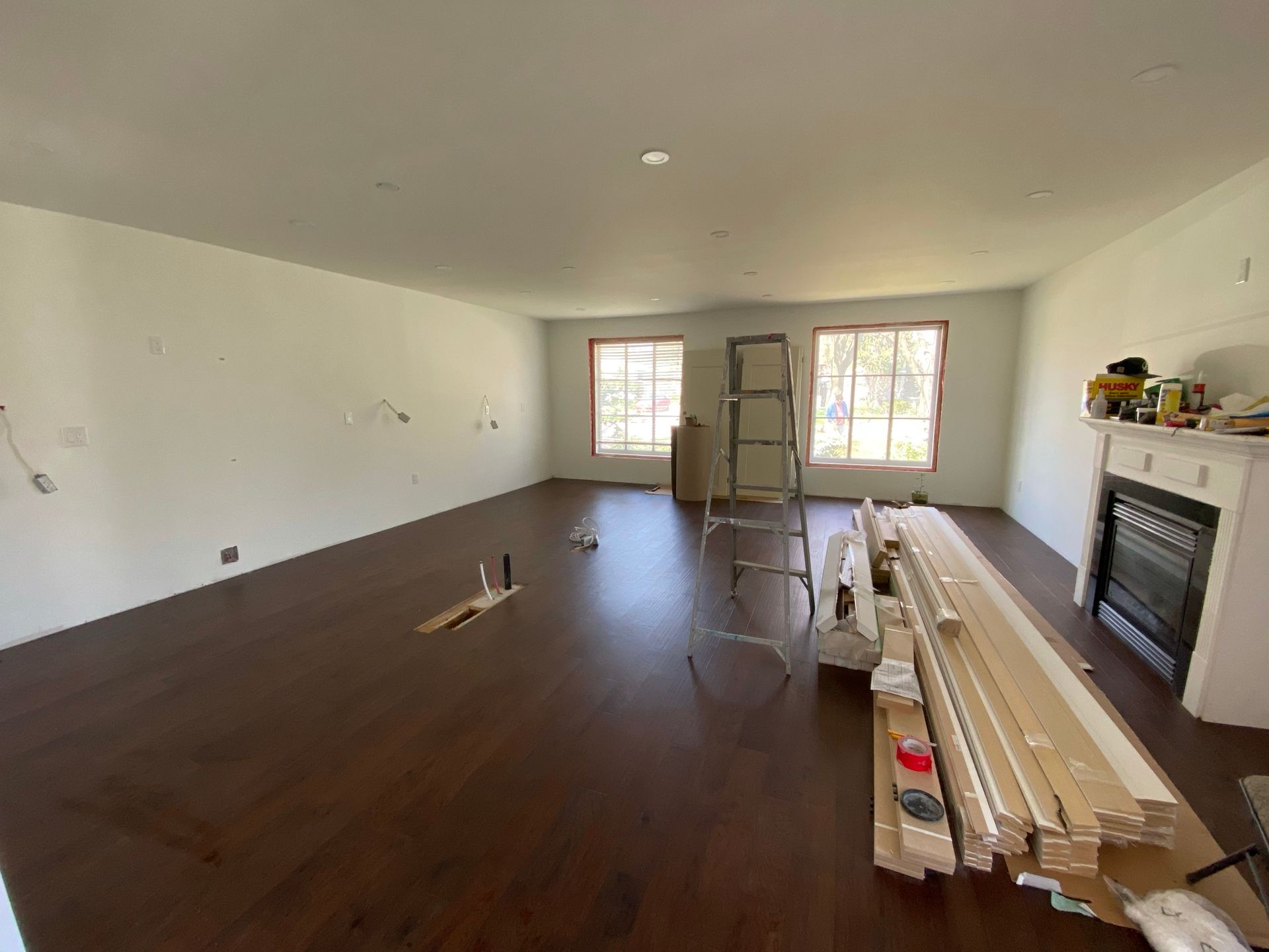 Empty living room with dark wood flooring, white walls, and fireplace under construction.
