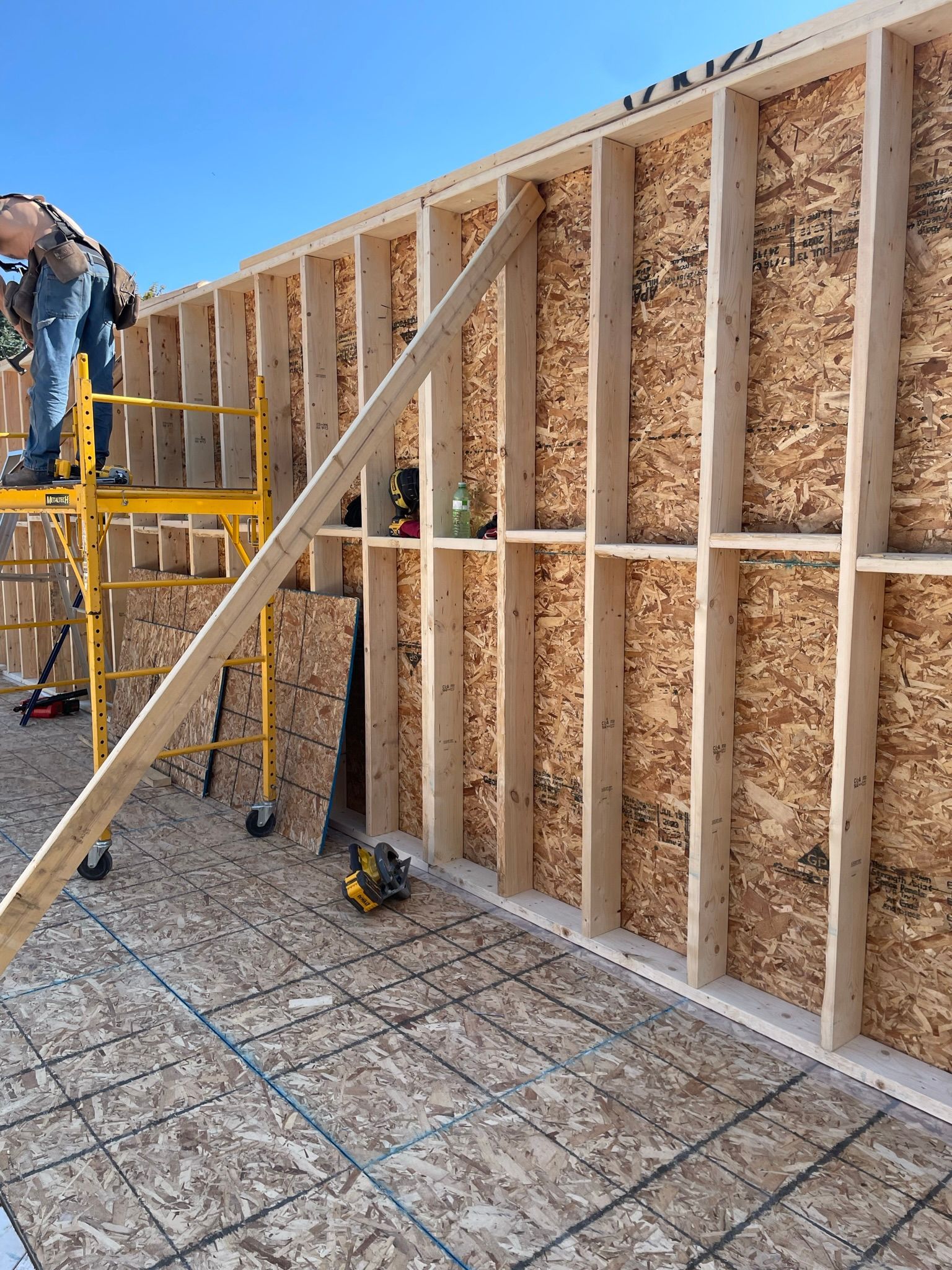 A man is standing on a scaffolding next to a wooden wall.