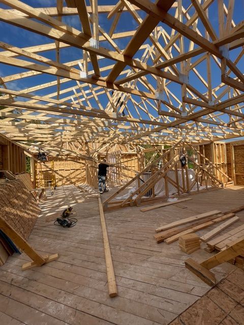 Construction site interior, wooden framing, rafters, a worker in a shirt and pants, blue sky.
