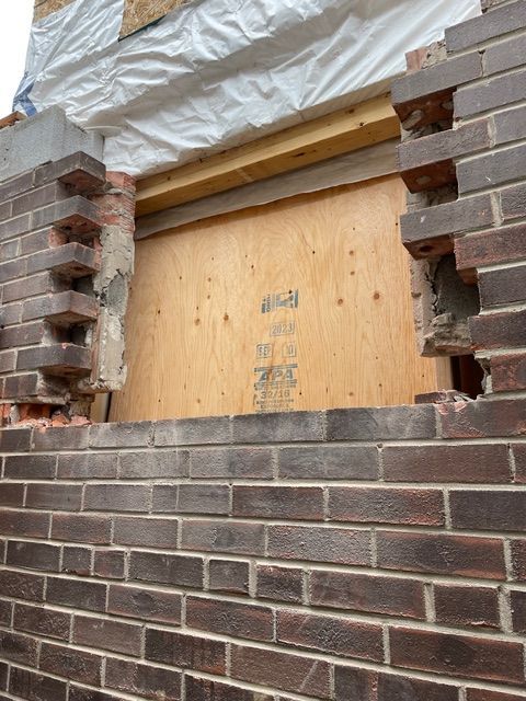 Brick wall with opening covered by plywood, revealing construction progress.